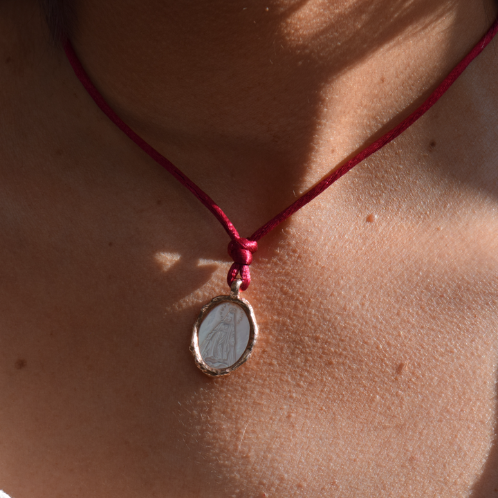Modelo luciendo medalla de la Virgen Milagrosa en nácar y oro rosa 18k con cordón rojo By Elena Carrera