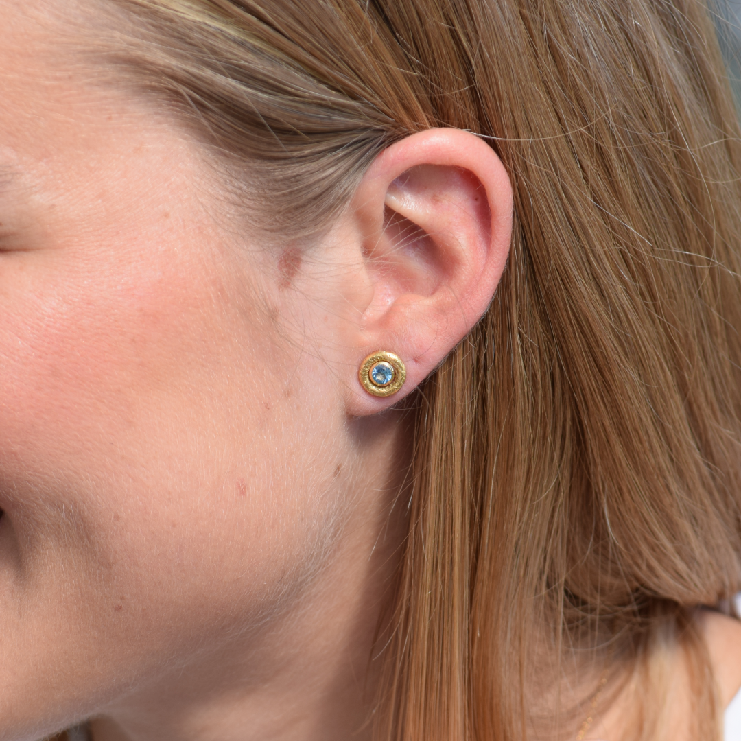 Modelo llevando pendientes de topacio azul y oro amarillo 18k y accesorio de oro amarillo 18k de By Elena Carrera